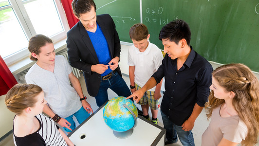 Schüler*innen stehen mit ihrem Lehrer im Kreis um einen Globus herum.