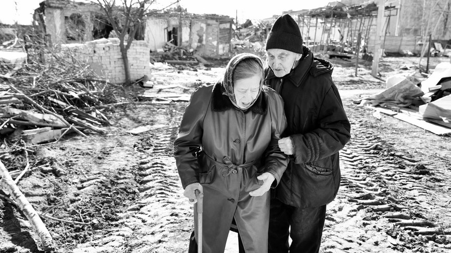 Frau und Mann aus der Ukraine stehen vor Trümmern.