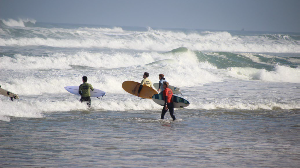 Menschen gehen mit Surfbrettern ins Wasser