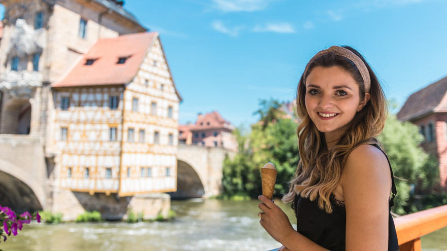 Eine Studentin isst Eis am Alten Rathaus – das Wahrzeichen von Bamberg ist in den Fluss Regnitz gebaut.