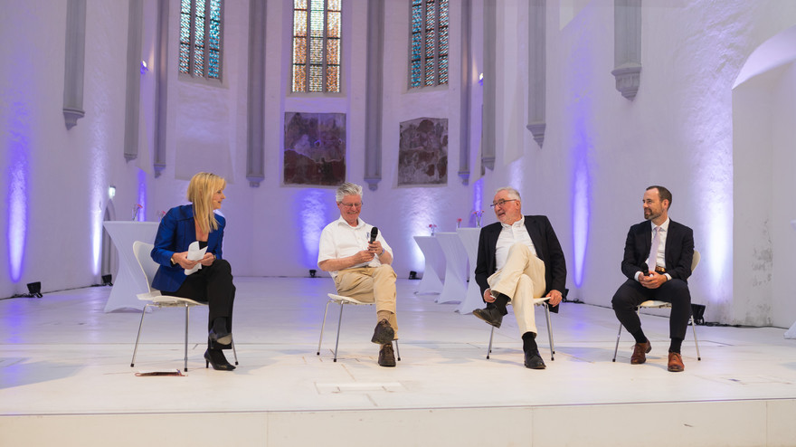 Maria Reinisch, Hartmut Graßl, Ernst Pöppel und Kai Fischbach sitzen auf der Bühne und diskutieren.