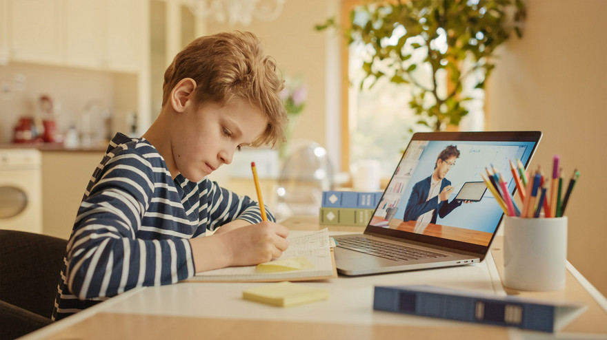 Junge beim Unterricht zu Hause am Schreibtisch vor dem aufgeklappten Laptop
