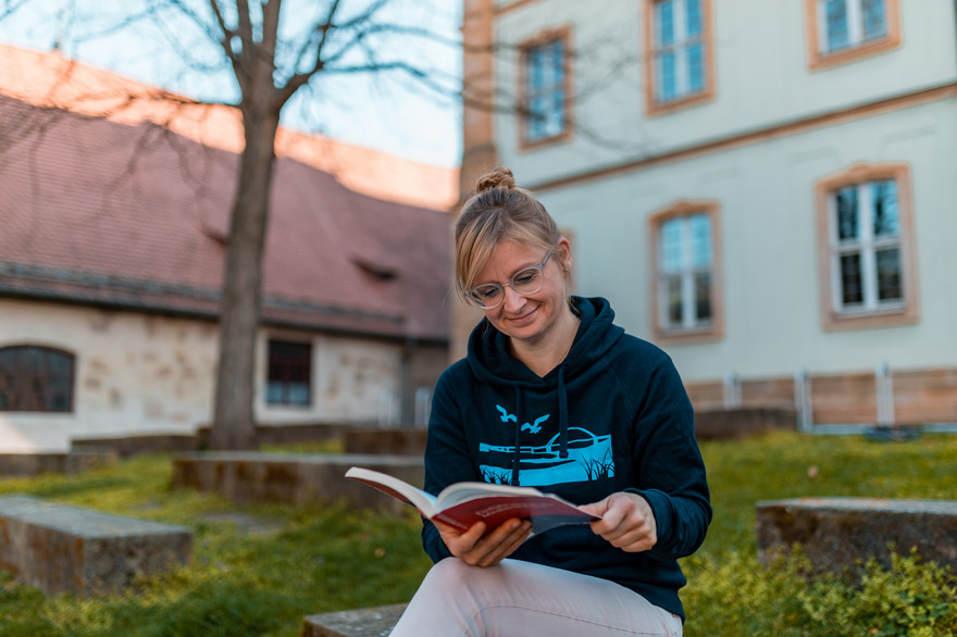 Annelie Faber sitzt lesend vor der Uni Bamberg.