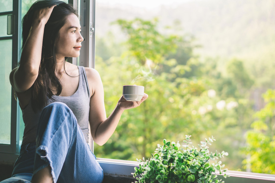 Frau sitzt am Fenster, trinkt einen Kaffe und genießt die Aussicht