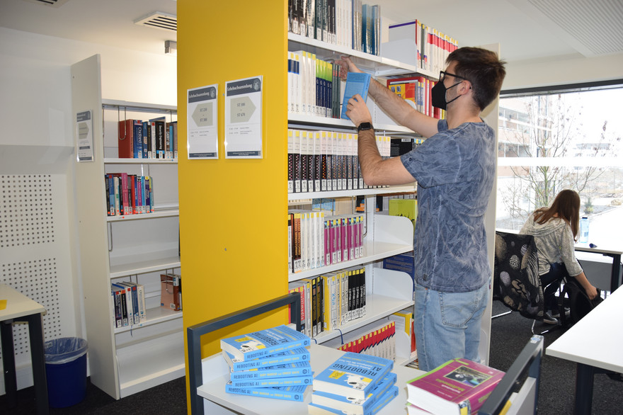 Mitarbeiter Leon Hehl räumt das Gewinnerbuch in ein Regal in der Universitätsbibliothek.