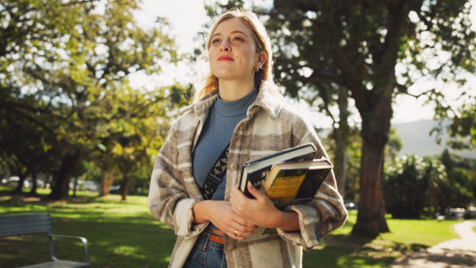 Student, woman and books in park for walk to class with education, learning or thinking for development at campus. Person, smile and vision on path, perspective and scholarship at college in Germany