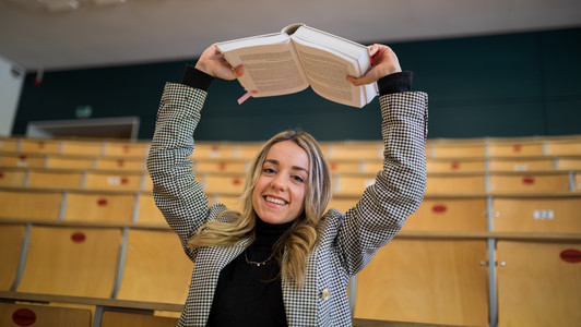 Studierende lacht und hält ein Buch in die Luft