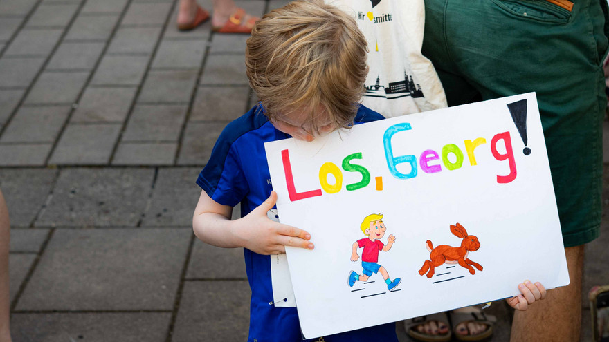 Kleiner Junge hält ein Schild mit der Aufschrift "Los Georg!"