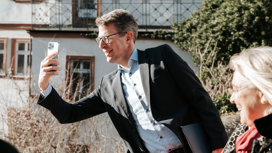 Wissenschaftsminister Markus Blume macht ein Selfie vor Bambergs Kulisse