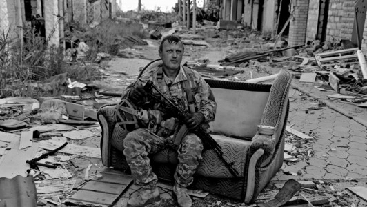 Ein ukrainischer Soldat sitzt auf einer Couch umgeben von Trümmern.