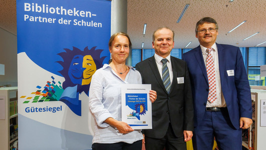 Dr. Fabian Franke (rechts im Bild) und Christiane Lauterbach von der Universitätsbibliothek Bamberg nahmen das Zertifikat aus den Händen von Ministerialdirektor Dr. Rolf-Dieter Jungk entgegen.