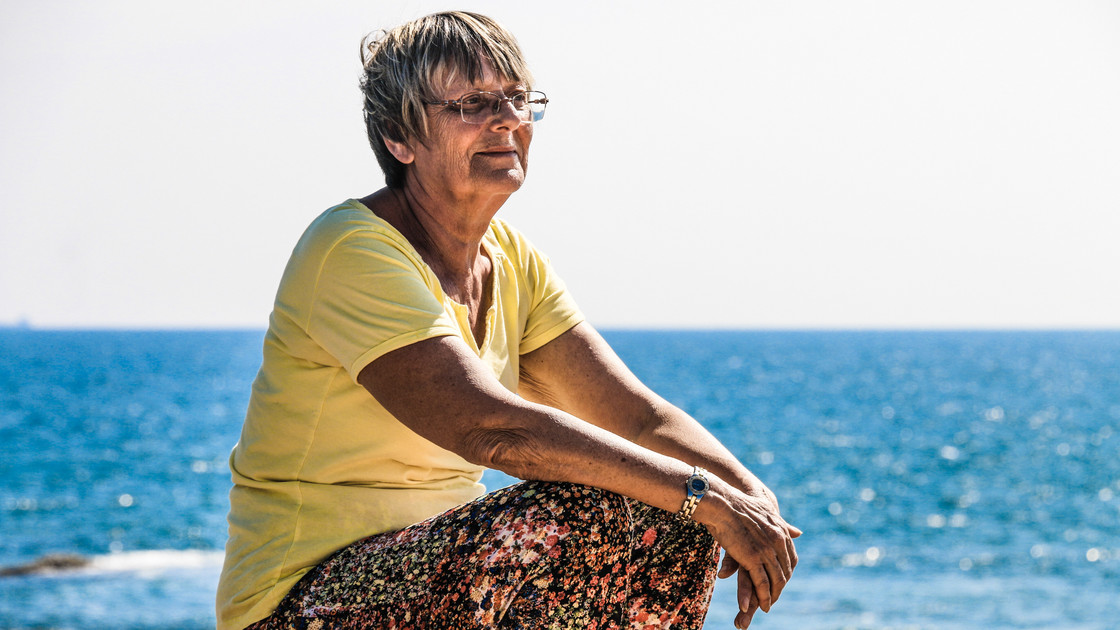 Ältere Frau sitzt am Meer und schaut in die Ferne.
